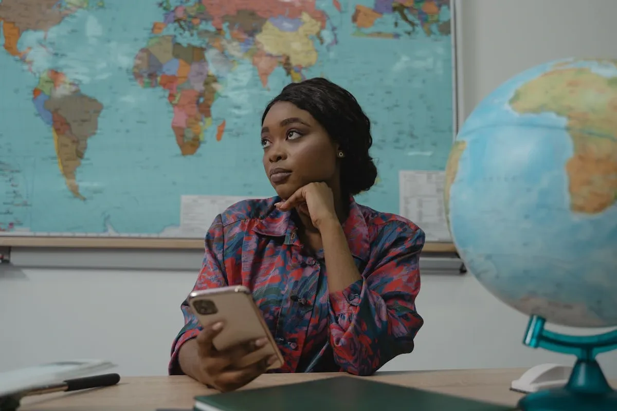 Female student using smartphone for language learning app with world map in background during study session